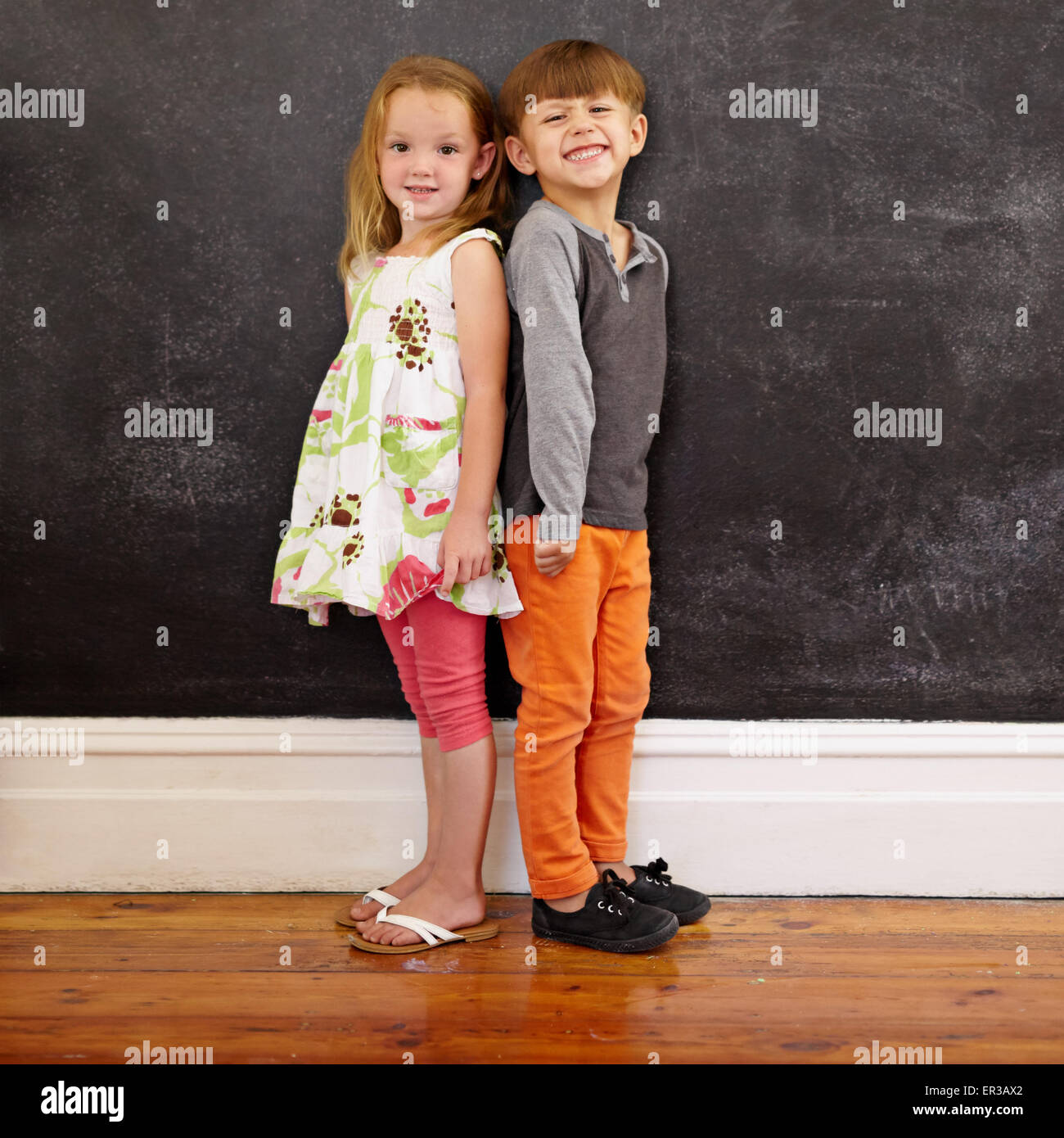 Little Boy and Girl standing in front of blackboard looking at camera de sourire. Longueur totale de l'image deux innocents li Banque D'Images