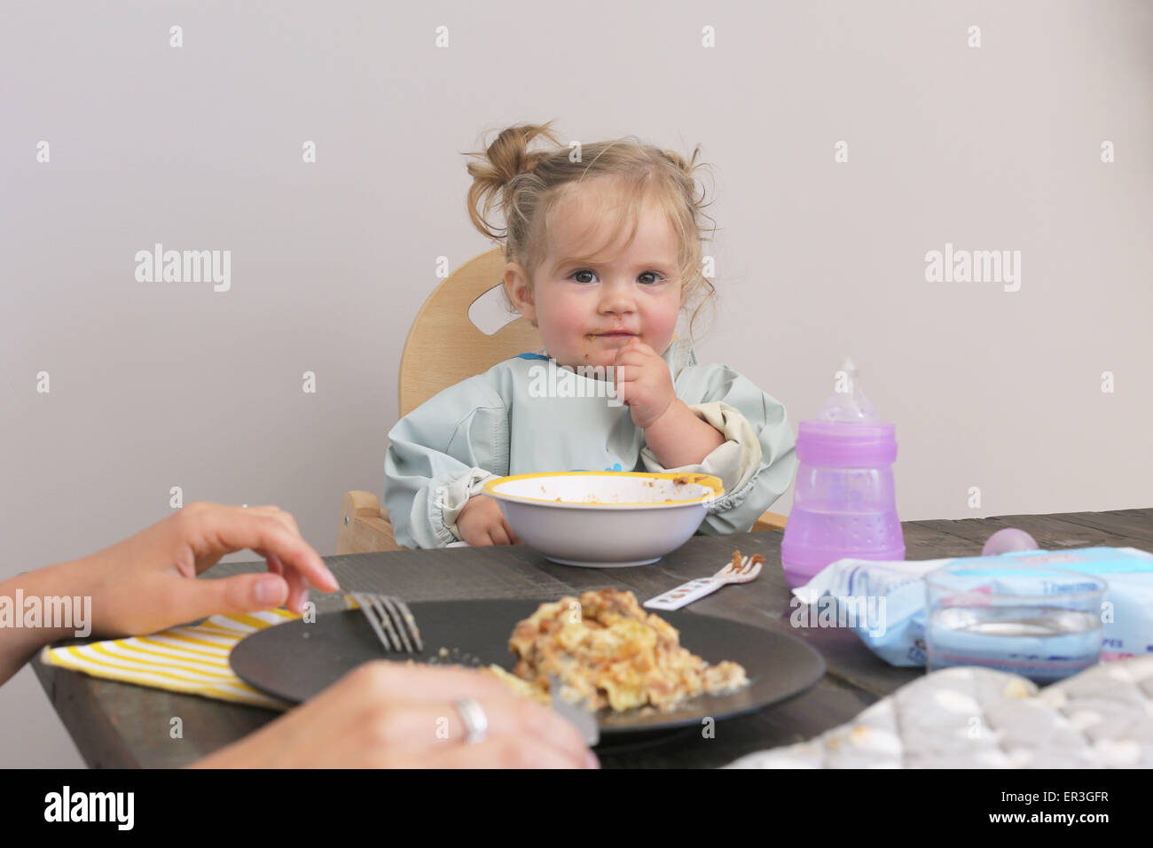 Bébé assis dans une chaise haute à la table having meal Banque D'Images