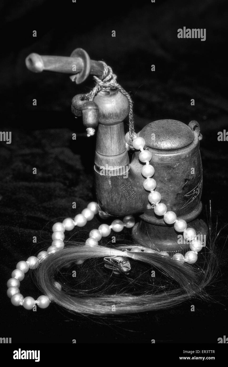 Still Life photo en noir et blanc d'un vintage, un tuyau allemande Garmisch pearl collier et une serrure des cheveux blonds. Fond noir Banque D'Images