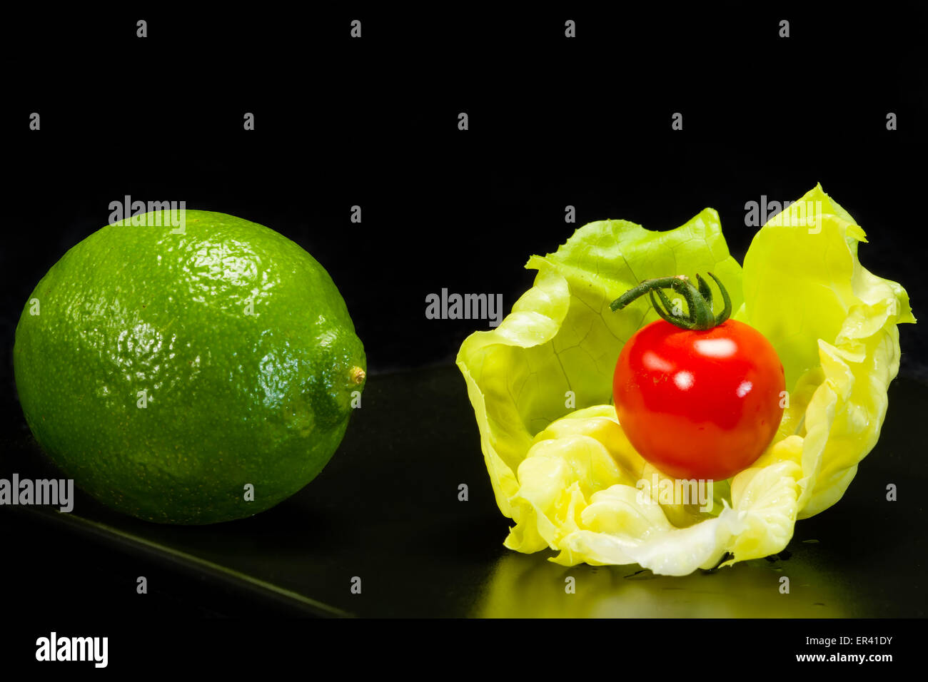 Laitue, tomate et citron vert sur un fond noir Banque D'Images
