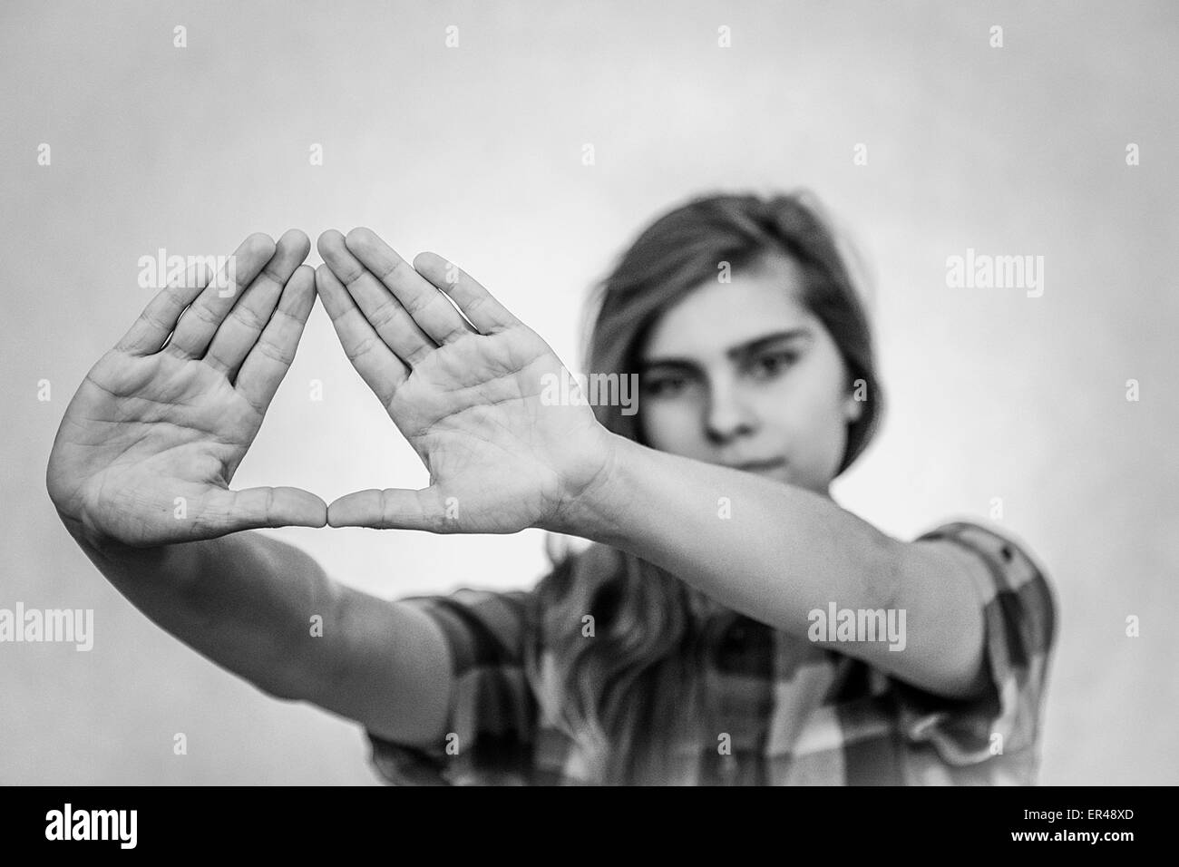 Jeune adolescente montrant le symbole triangle Illuminati. Fond blanc derrière elle. Banque D'Images