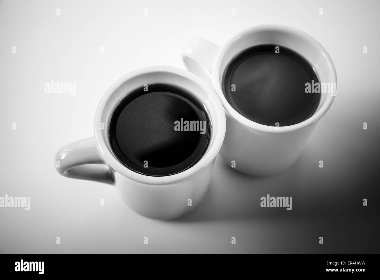 Deux tasses de café plein debout sur une table avec l'ombre noire, monochrome photo stylisée Banque D'Images