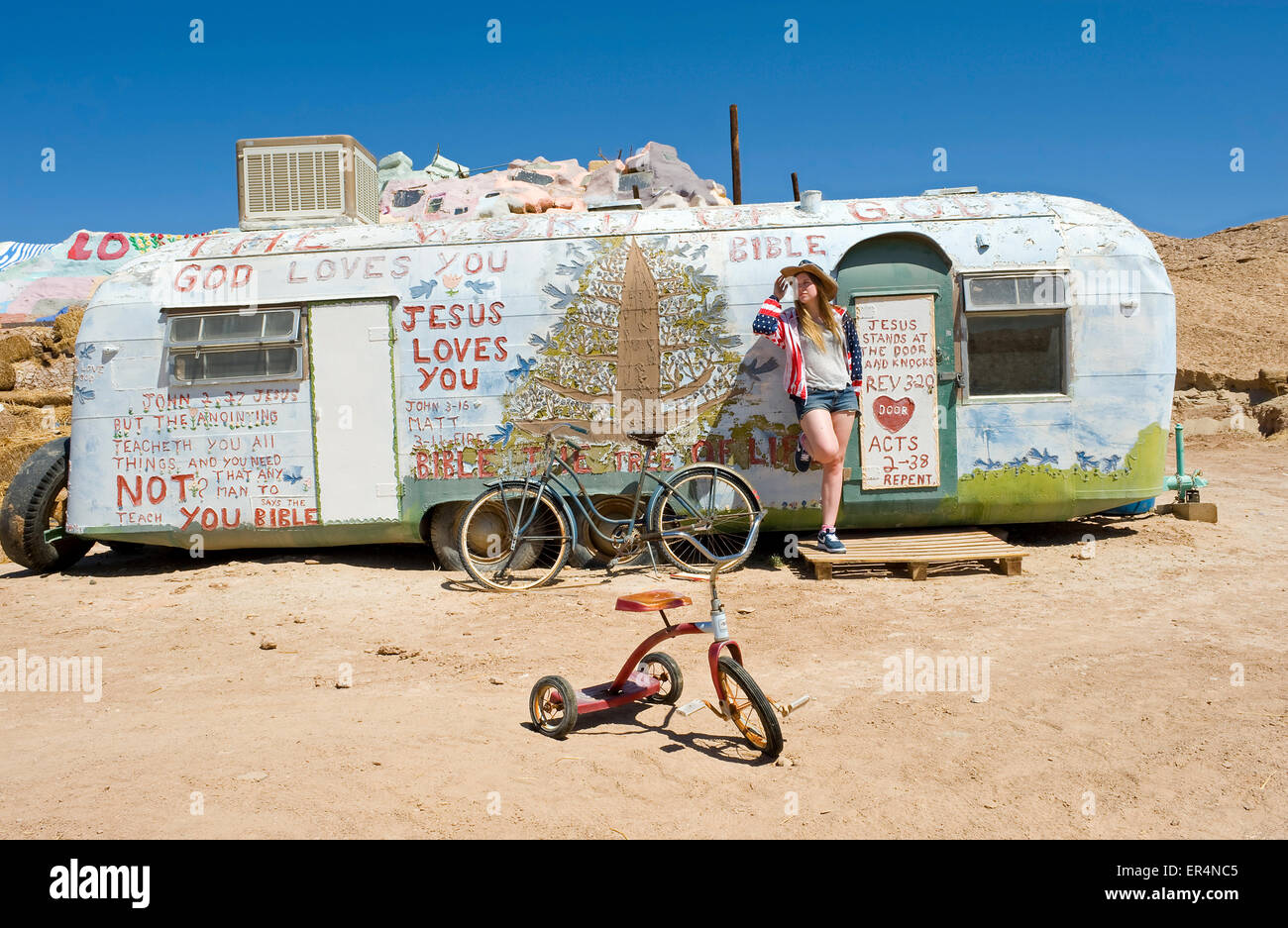 Fille dans stars and stripes veste et hat standing près de tricycle avec remorque derrière, salut Mont créé par Leonard Knight. Banque D'Images