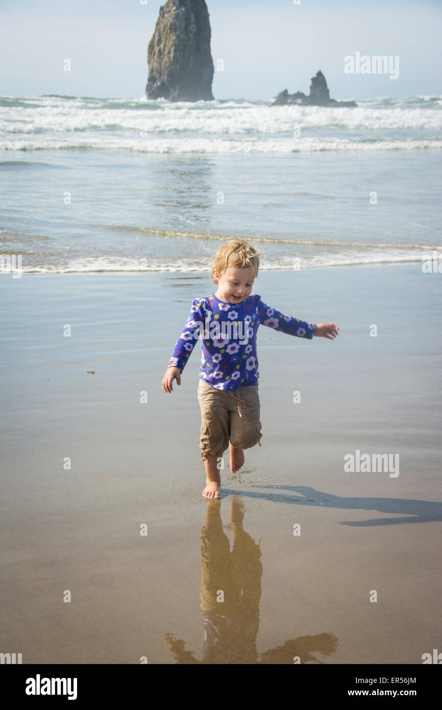 Bébé fille s'étend de l'océan vagues sur Cannon Beach, Oregon. Banque D'Images