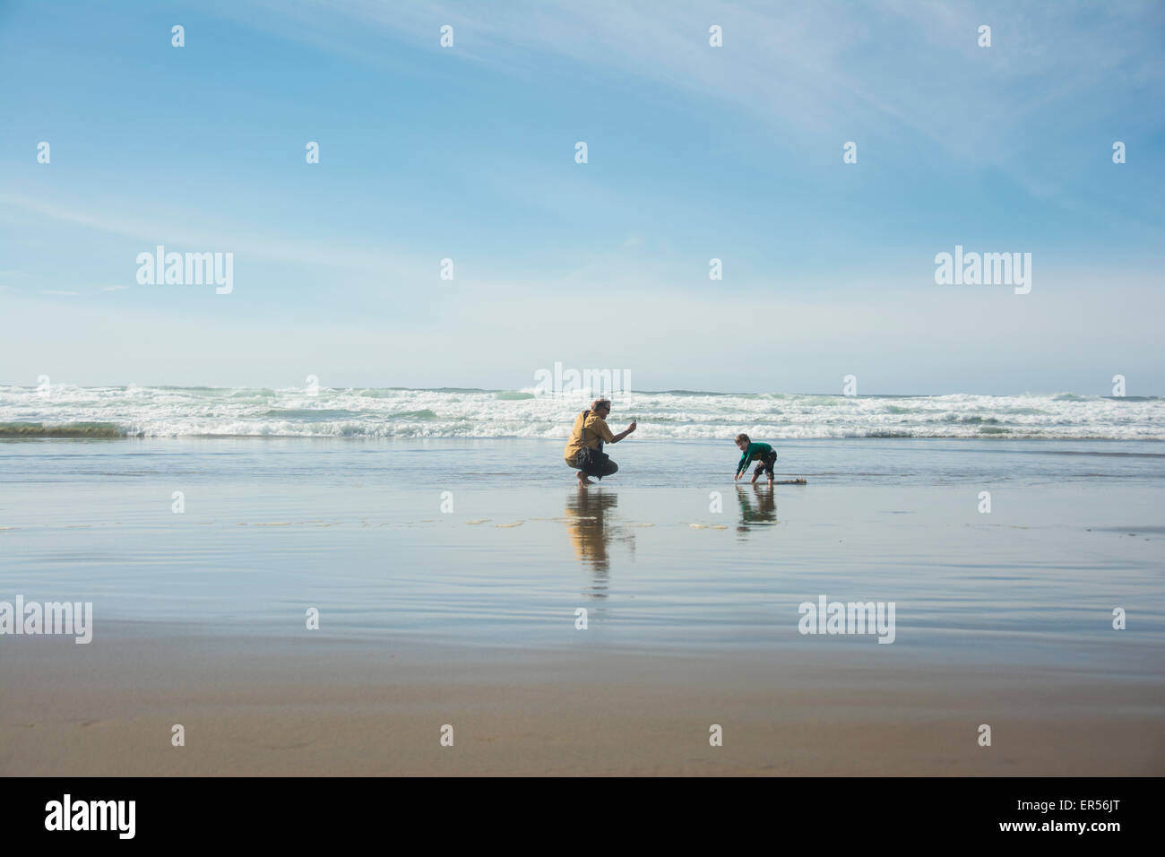 Père prend photo avec téléphone portable de petit garçon de creuser dans le sable, Cannon Beach, Oregon. Banque D'Images