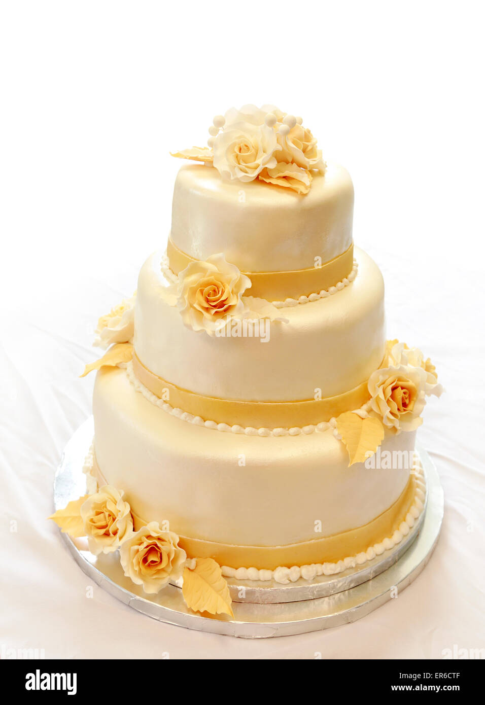 Gâteau de mariage. 3-niveaux couverts de l'ivoire du fondant pulvérisés avec spray pearl jaune/or et roses de sucre Banque D'Images