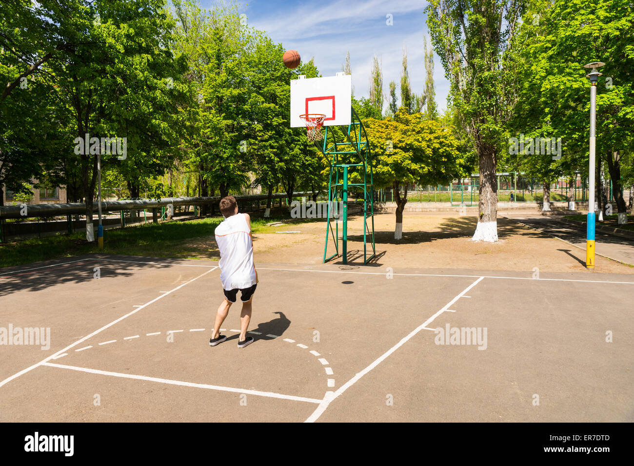 Jeune homme athlétique en tenant tourné sur panier du haut de la clé sur un terrain de basket-ball dans le parc verdoyant Banque D'Images
