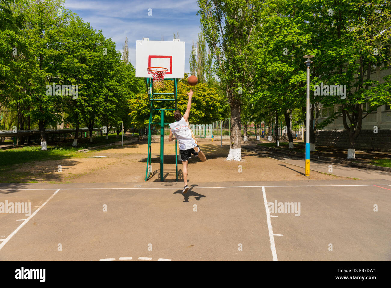 Jeune homme athlétique qui pondent jusqu'tourné sur le panier de basket dans le parc verdoyant Banque D'Images