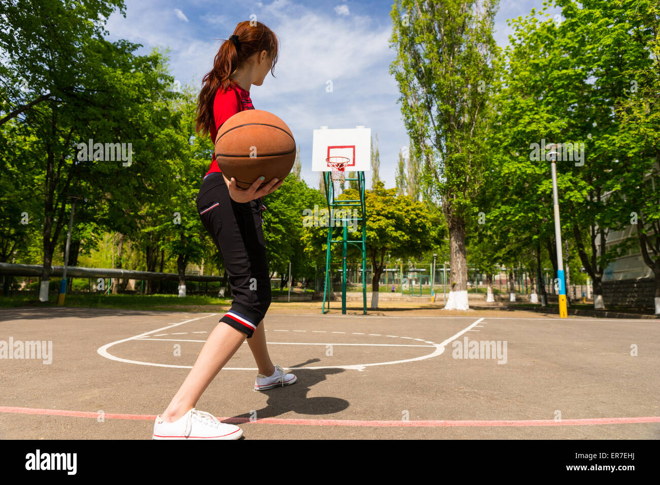Vue arrière sur toute la longueur des jeunes Athletic Woman Holding Basket-ball, se préparant à jeter au panier Ballon libre du haut de la clé sur un terrain de basket-ball. Banque D'Images