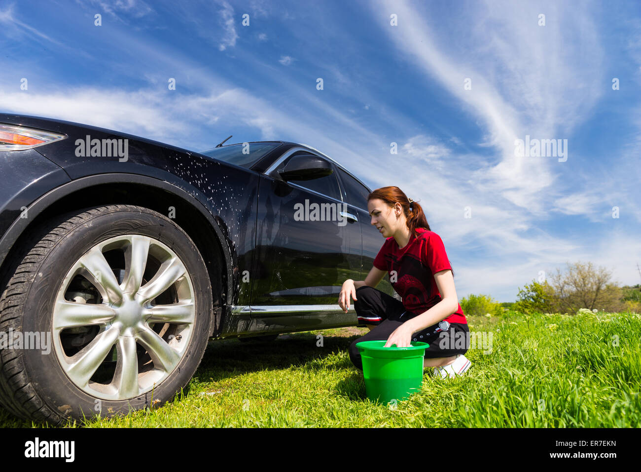 Femme avec godet Vert Noir Lavage véhicule de luxe avec une éponge savonneuse en vert sur champ journée ensoleillée avec ciel bleu Banque D'Images