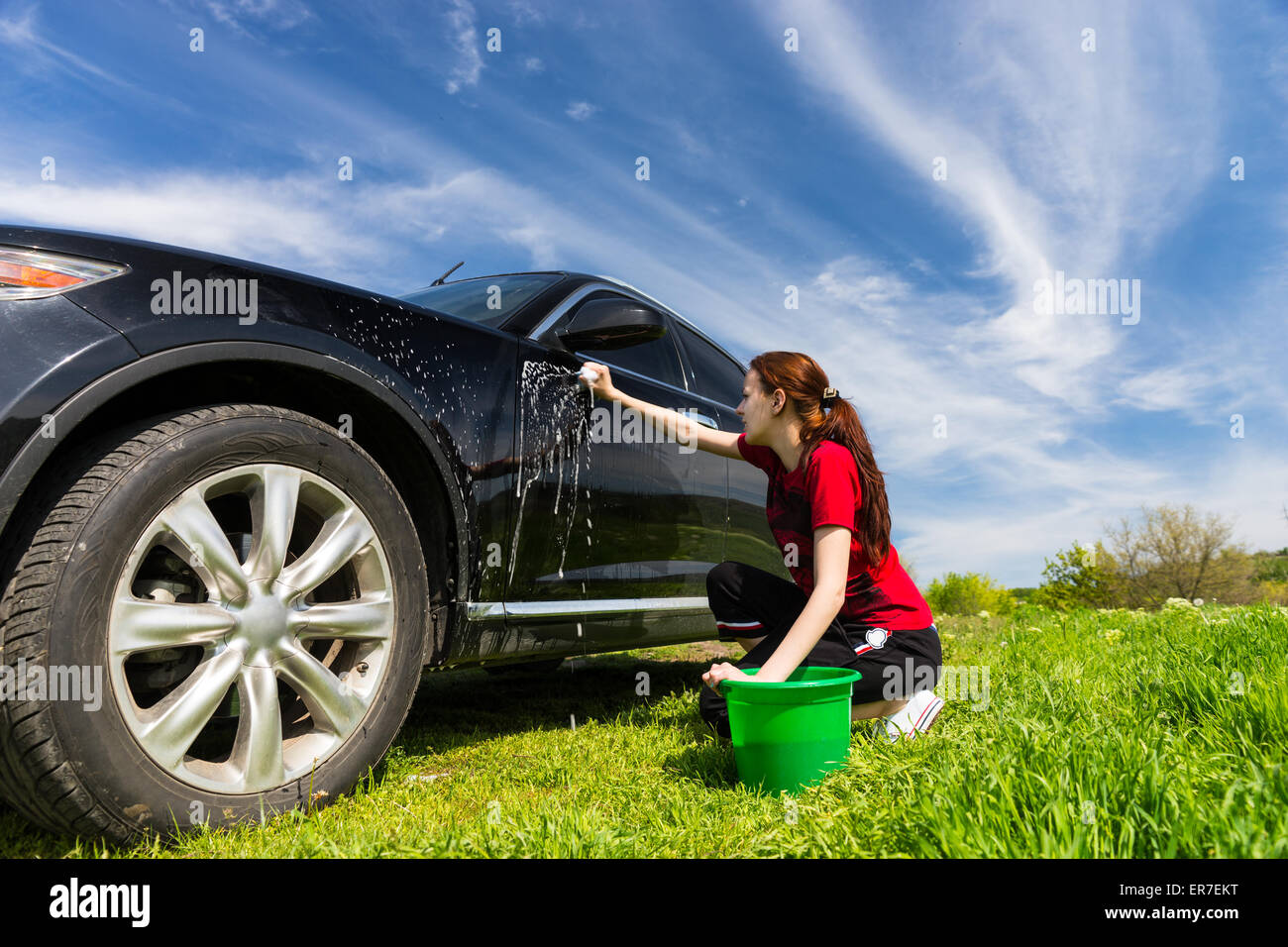 Femme avec godet Vert Noir Lavage véhicule de luxe avec une éponge savonneuse en vert sur champ journée ensoleillée avec ciel bleu Banque D'Images