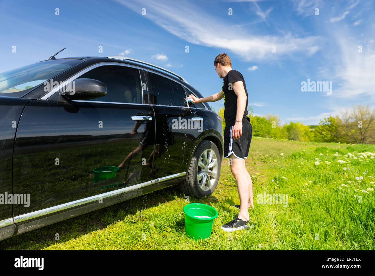 La longueur totale de l'homme lave voiture avec une éponge savonneuse en vert sur le terrain herbeux journée ensoleillée avec ciel bleu Banque D'Images