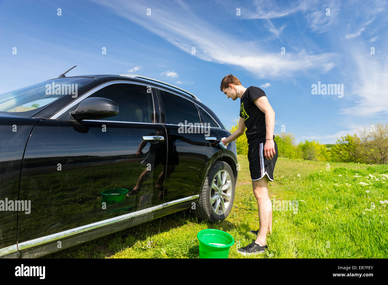 La longueur totale de l'homme lave voiture avec une éponge savonneuse en vert sur le terrain herbeux journée ensoleillée avec ciel bleu Banque D'Images