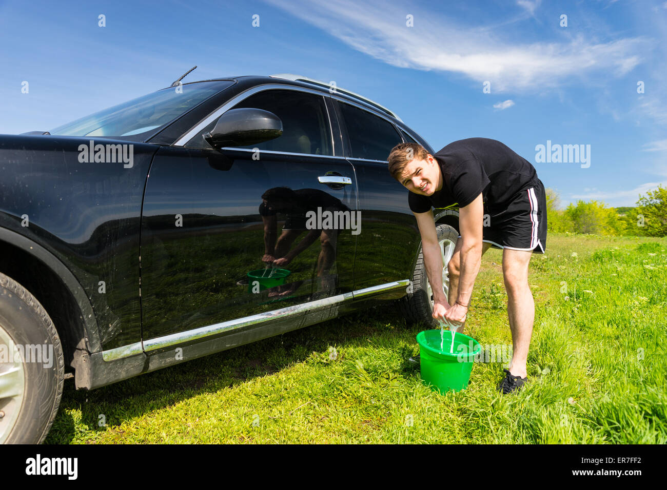L'homme à la caméra et à l'essorage de l'Éponge savonneuse dans la benne verte pendant le lavage de véhicules de luxe noir en vert les champs o Banque D'Images