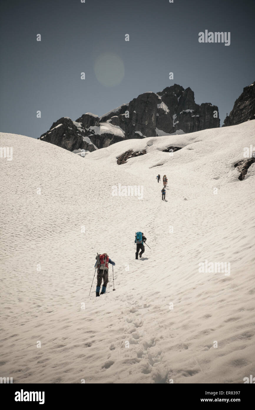 Six grimpeurs traversent un snow patch en route pour gravir le Pic Trio en Colombie-Britannique, Canada. Banque D'Images