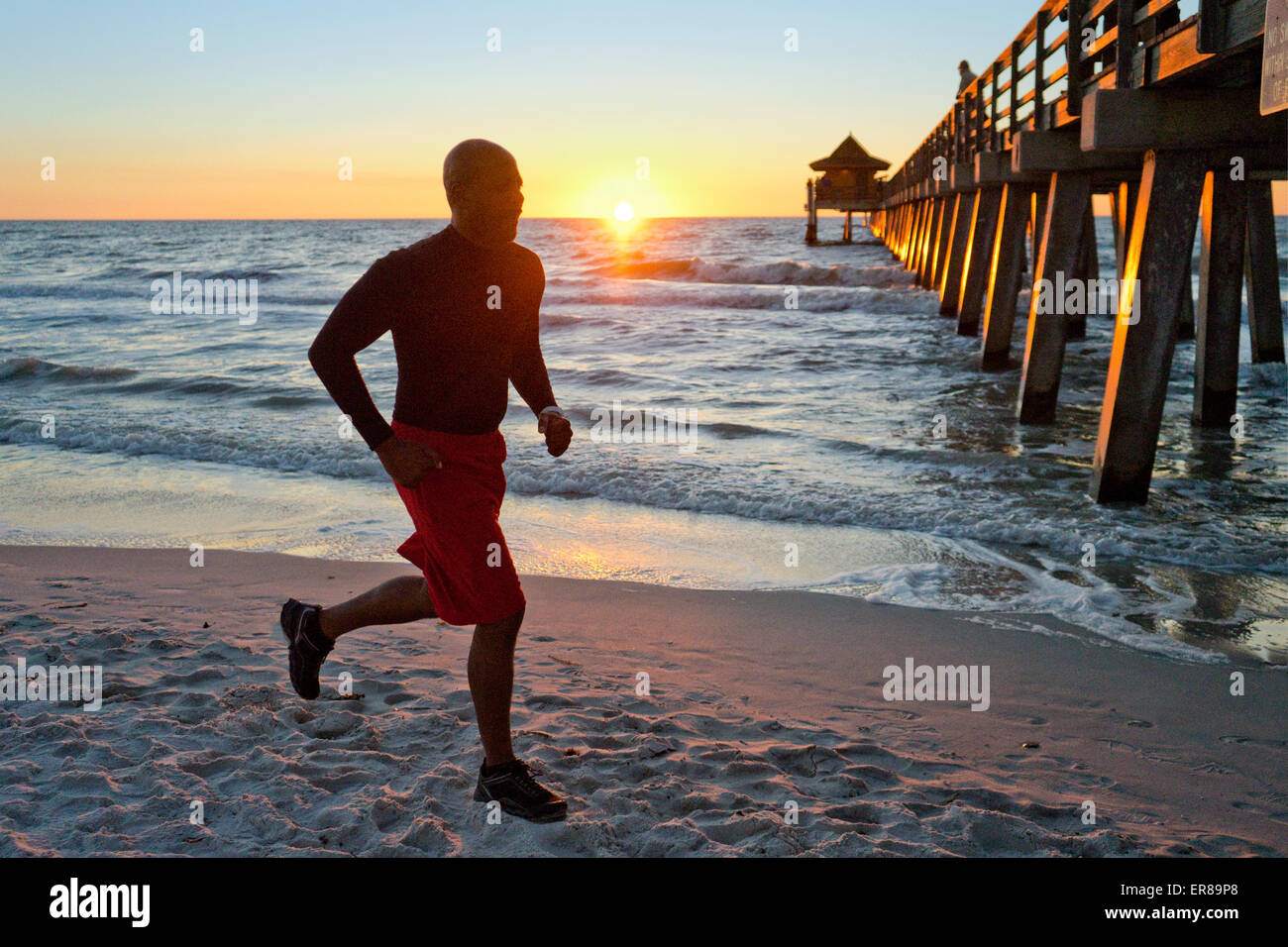 Homme qui court sur la plage au coucher du soleil Banque D'Images