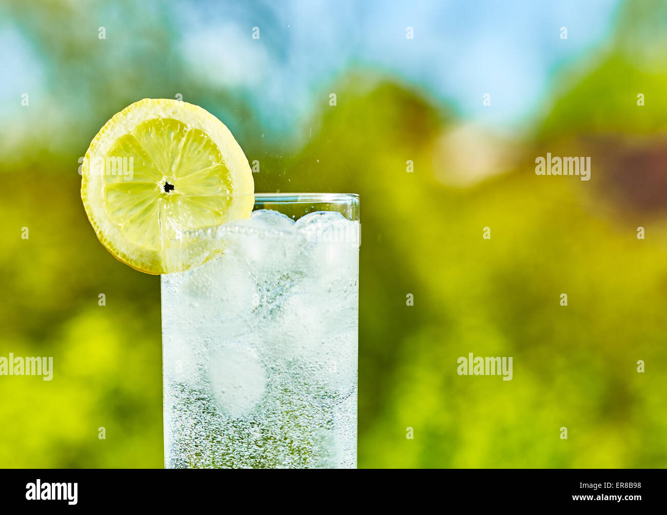 L'eau pétillante et tranche de citron sur le verre avec une glace, journée ensoleillée - focalisation étroite sur milieu de la vitre Banque D'Images
