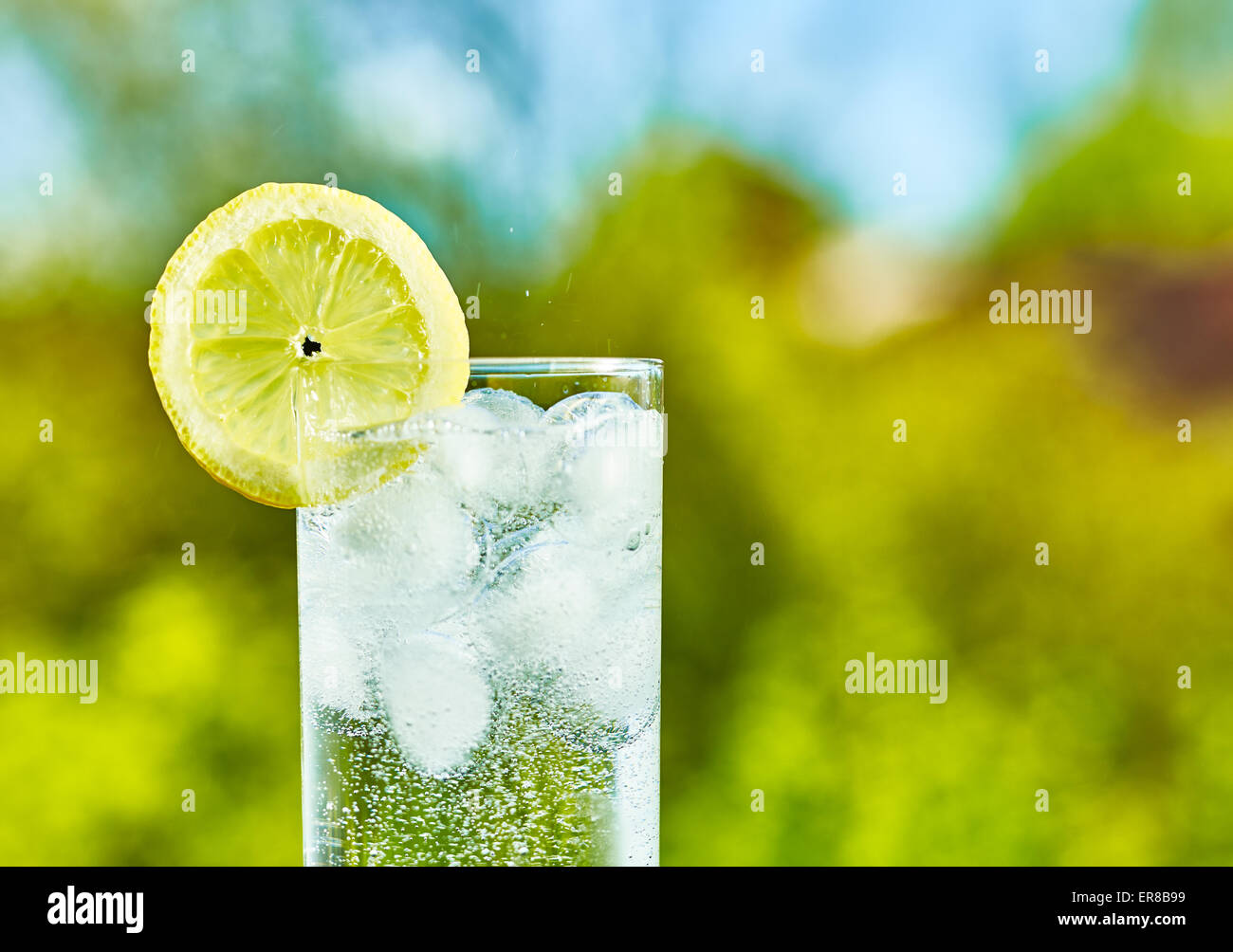 L'eau pétillante et tranche de citron sur le verre avec une glace, journée ensoleillée - focalisation étroite sur milieu de la vitre Banque D'Images
