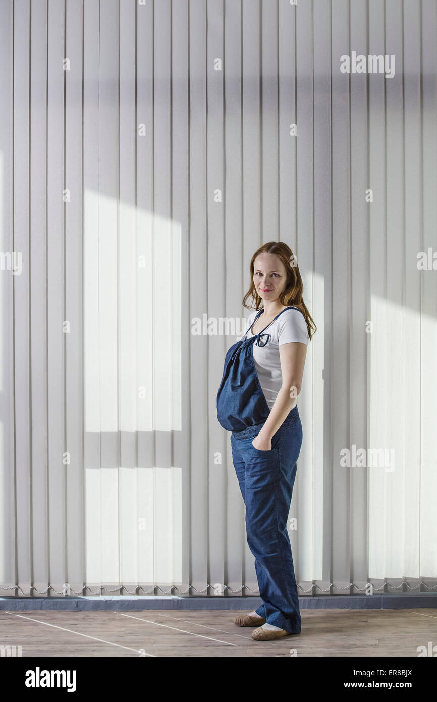 Portrait de femme enceinte en salopette debout contre curtain Banque D'Images