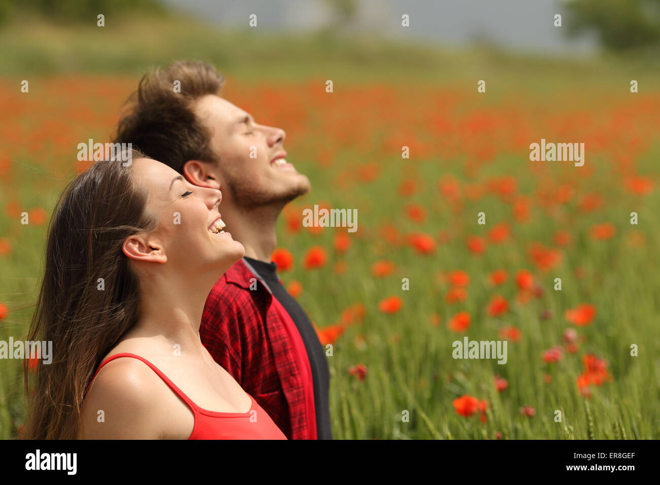 Couple heureux de respirer l'air frais dans un champ coloré avec des fleurs de pavot rouge Banque D'Images