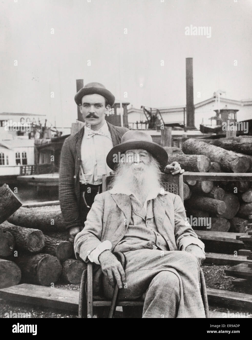 Walt Whitman avec son infirmière Warren Fritzenger, debout, et une pile de journaux derrière lui, sur le quai, probablement près de sa maison de la rue Mickle à Camden. 1890 Banque D'Images