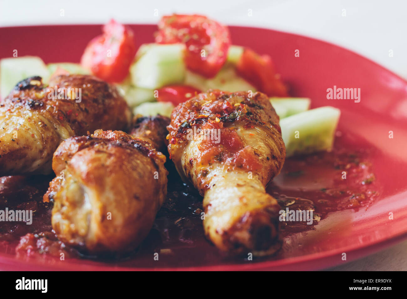 Cuisses de poulet rôti bio faits maison avec des épices servi sur assiette rouge Banque D'Images