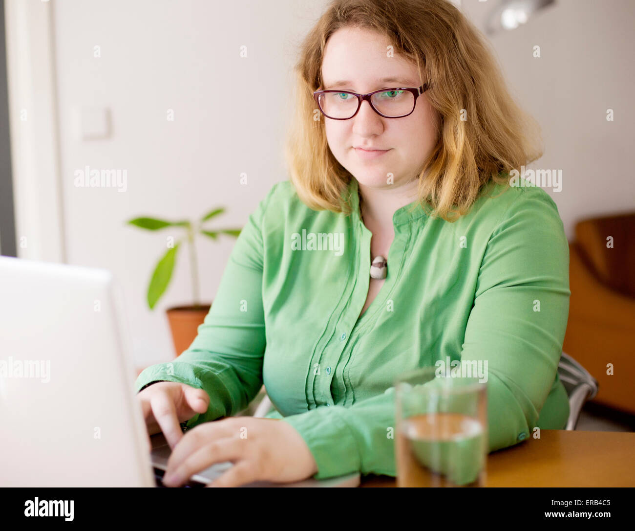 Jeune femme assise sur un bureau avec ordinateur portable et lunettes Banque D'Images