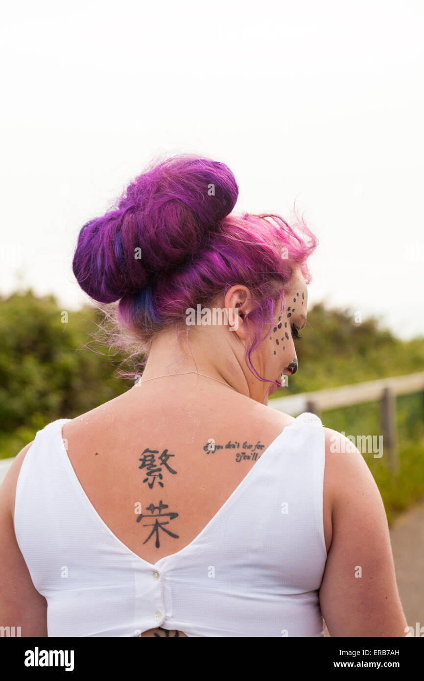 Femme avec des tatouages sur le dos, rouge, les cheveux en chignon et visage peint à Bournemouth en mai Banque D'Images