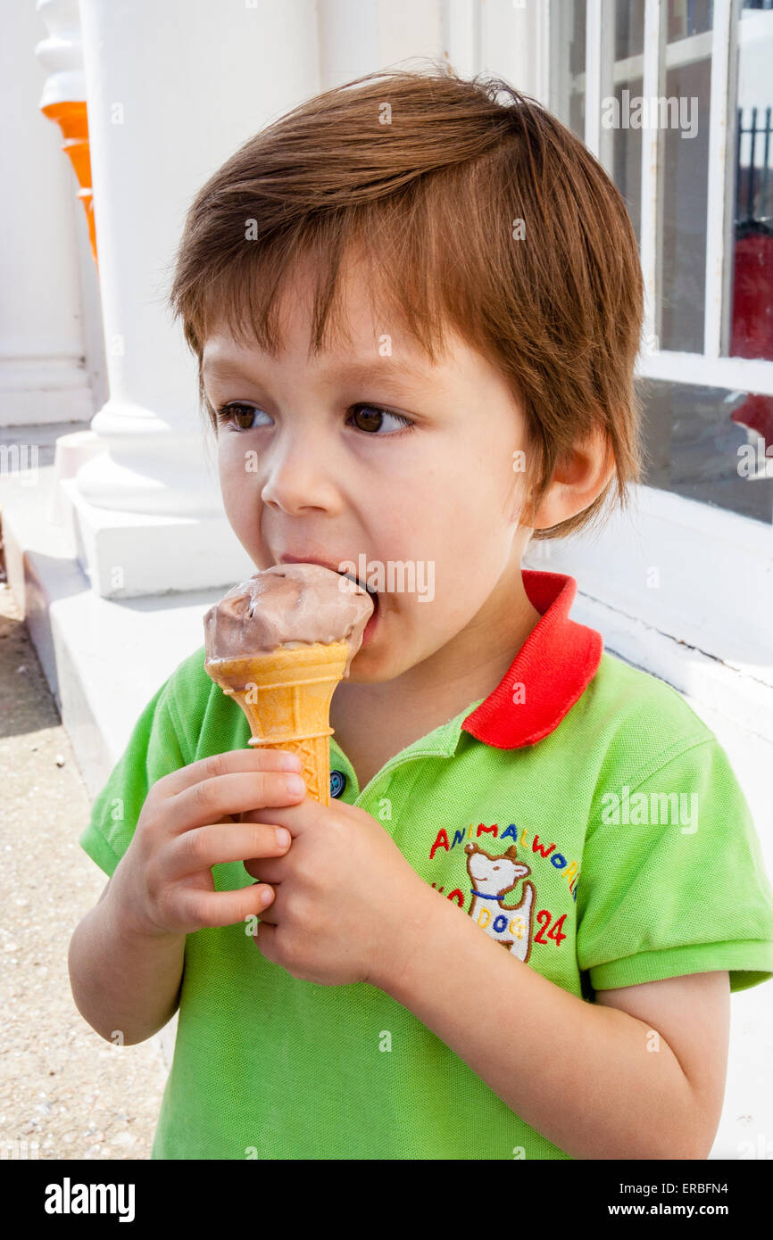 Enfant, garçon, 3 à 4 ans, extérieur, tenant le cône de glace dans les deux mains et se mordant au bord du cône et de la glace. Tir sur la tête et l'épaule. Banque D'Images