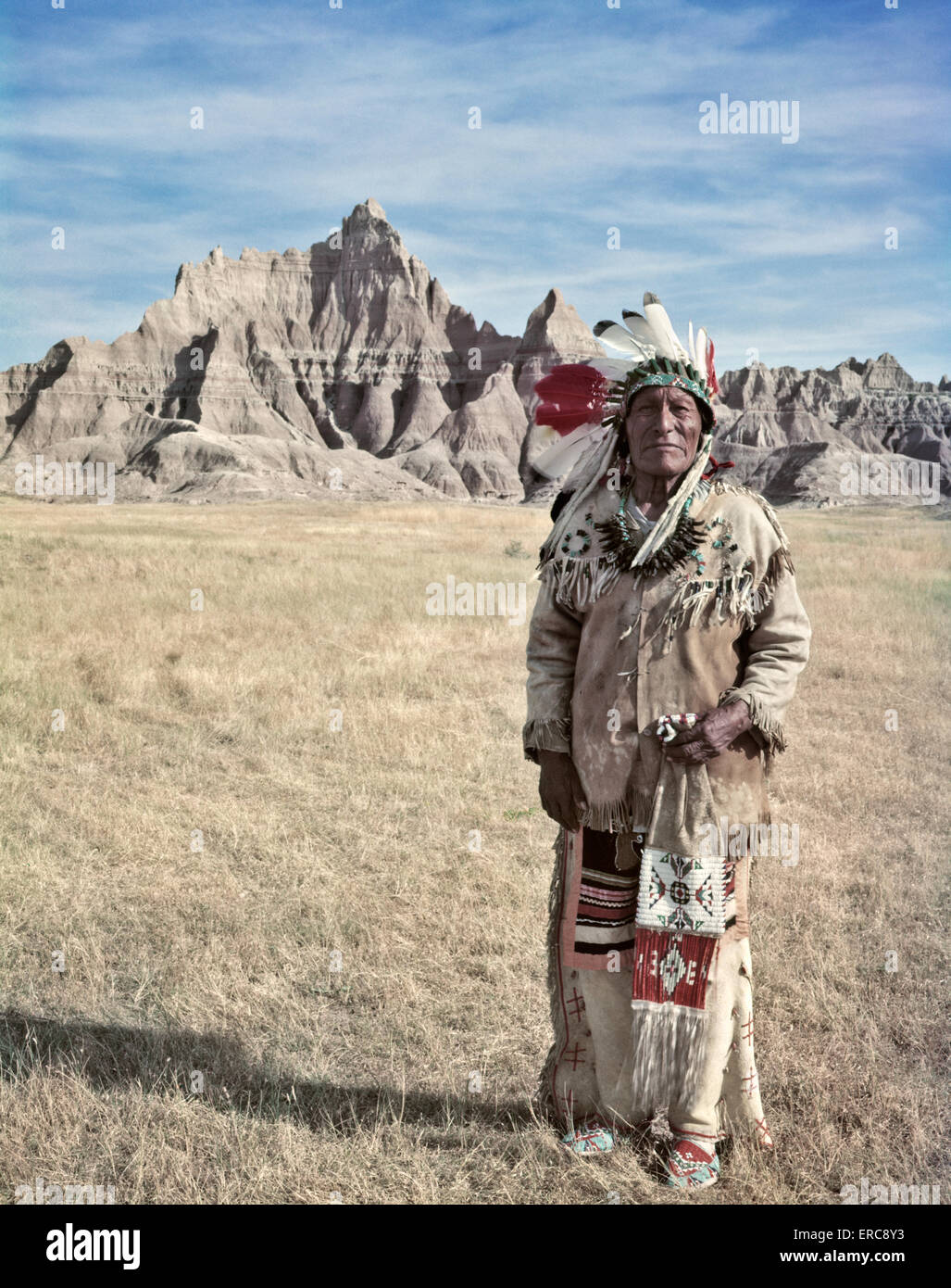 1950 PORTRAIT SIOUX INDIAN MAN STANDING IN BADLANDS DU DAKOTA DU SUD PORTANT DES NATIVE AMERICAN DRESS LOOKING AT CAMERA Banque D'Images