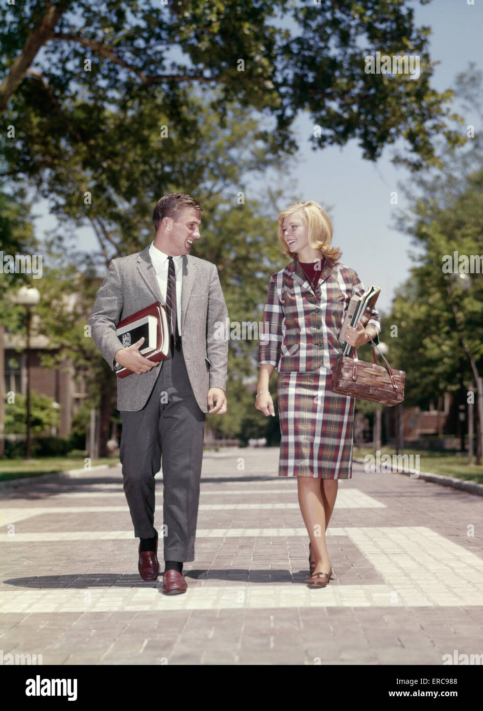 1960 JEUNE ADULTE HOMME FEMME marchant côte à côte sur COLLEGE CAMPUS SMILING HAPPY Banque D'Images