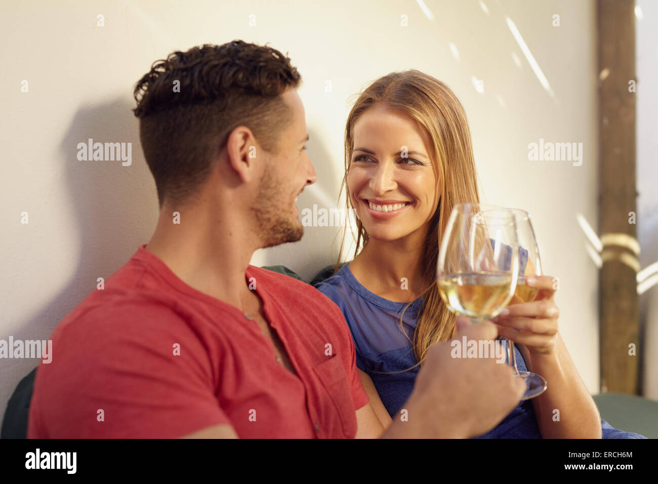 Heureux jeune homme et femme buvant un verre de vin dans leur arrière-cour. Couple toasting with wine and smiling. Banque D'Images