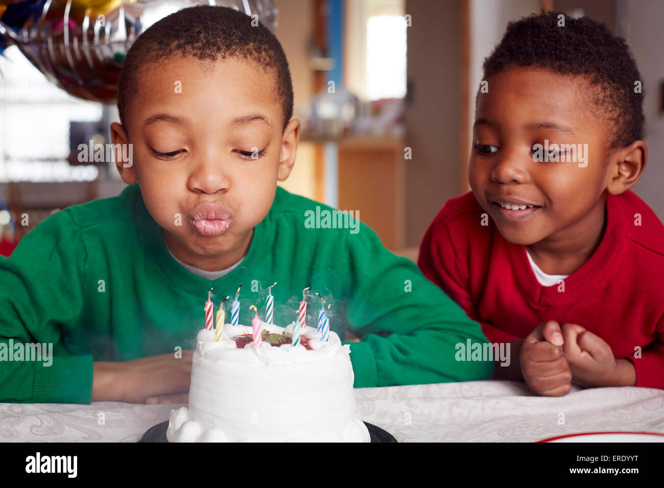 Black Boy blowing out candles cake at party Banque D'Images