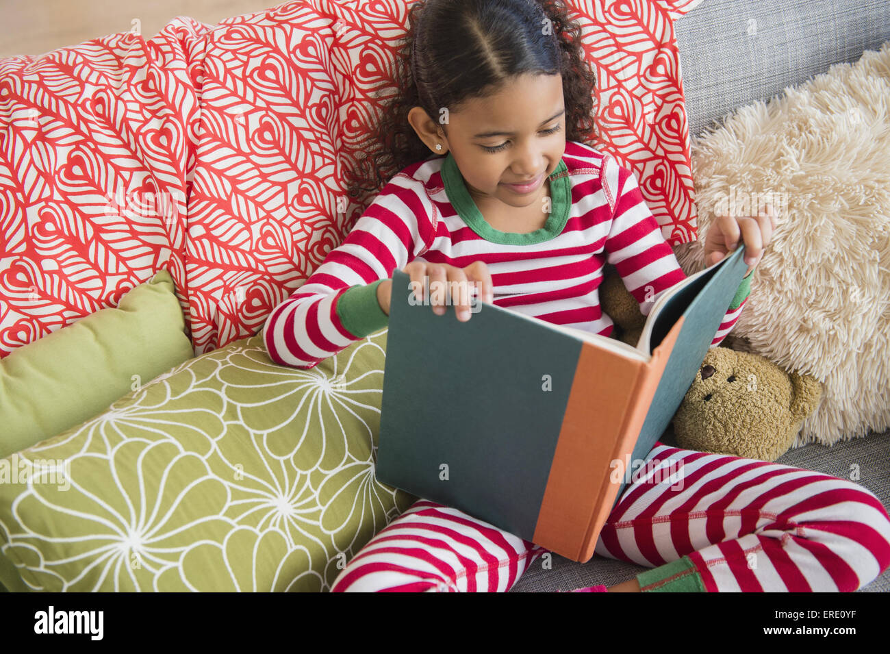 Mixed Race girl reading book on sofa Banque D'Images