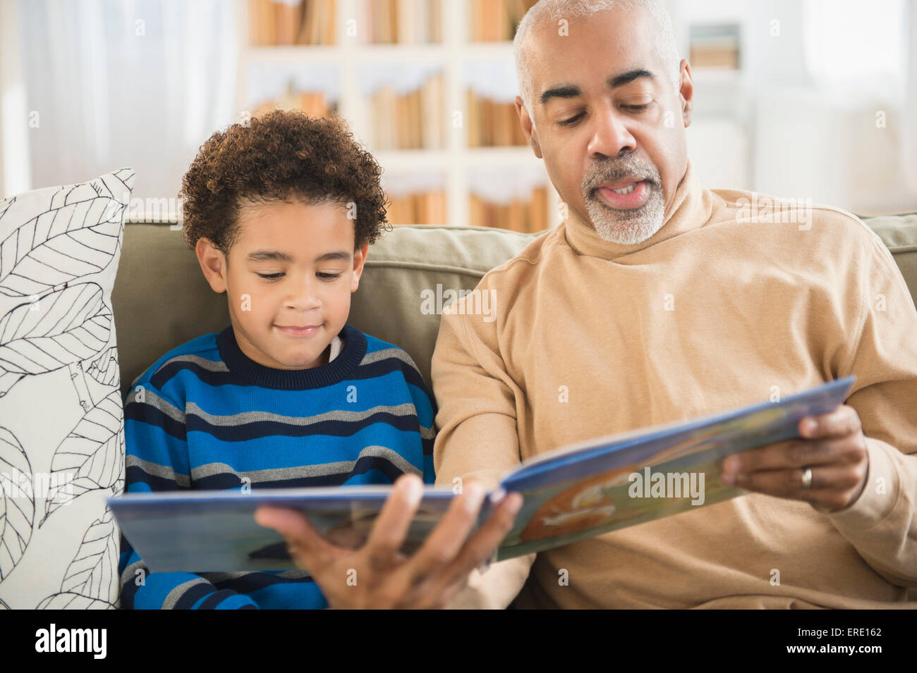 Mixed Race grand-père et petit-fils lecture livre sur canapé Banque D'Images