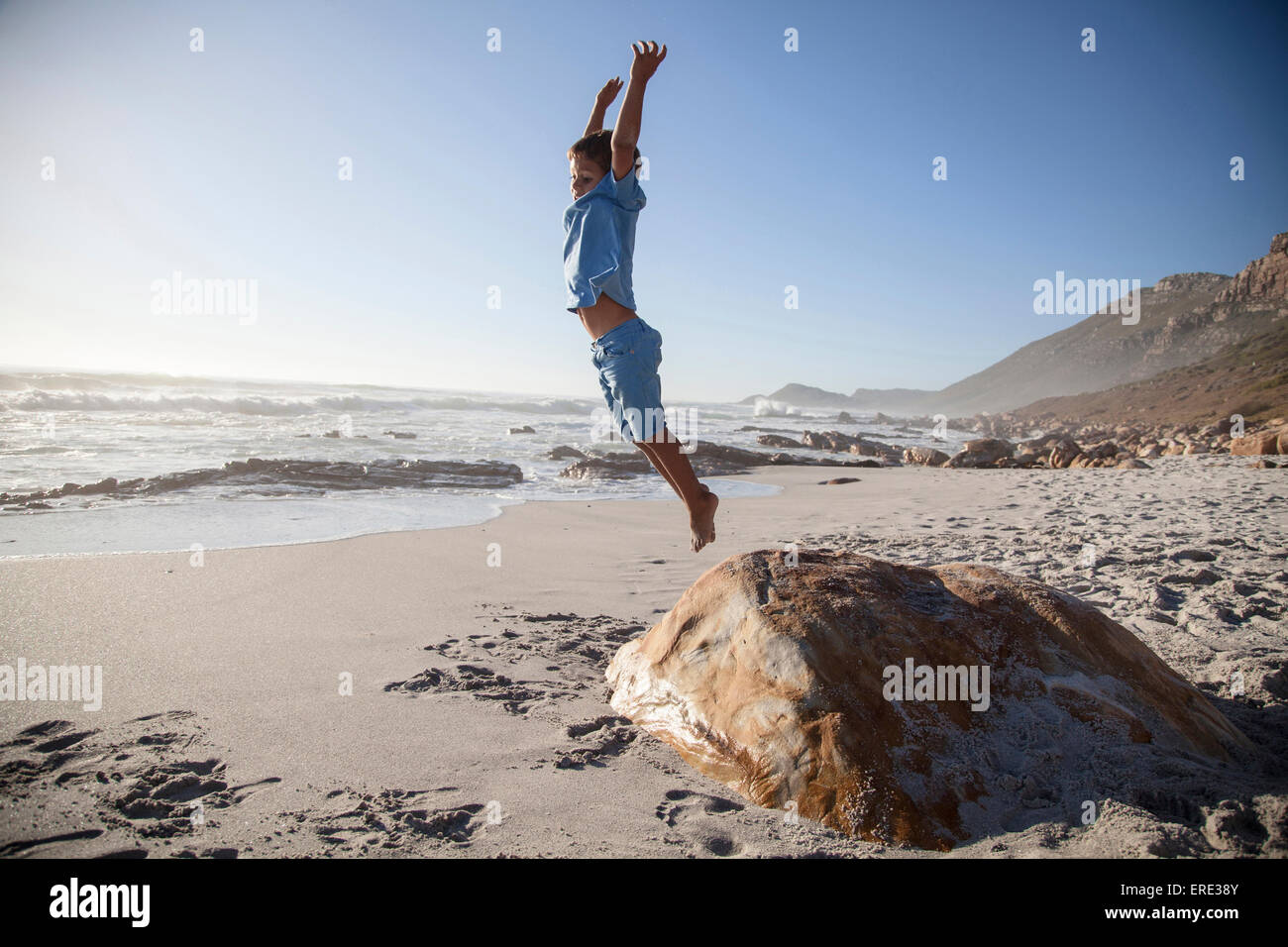 Mixed Race boy Jumping off rocher sur la plage Banque D'Images