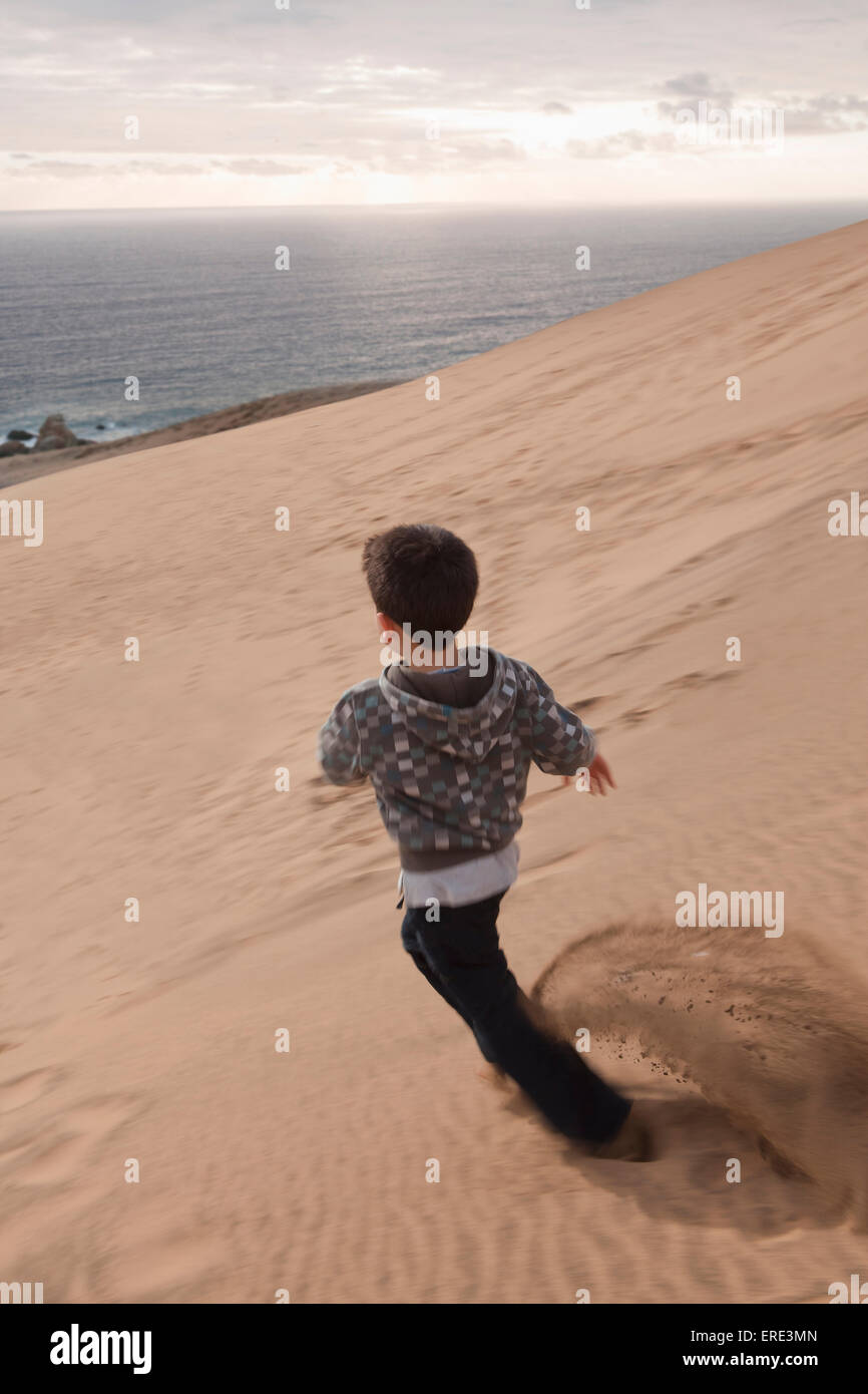 Hispanic boy running on sand dune on beach Banque D'Images