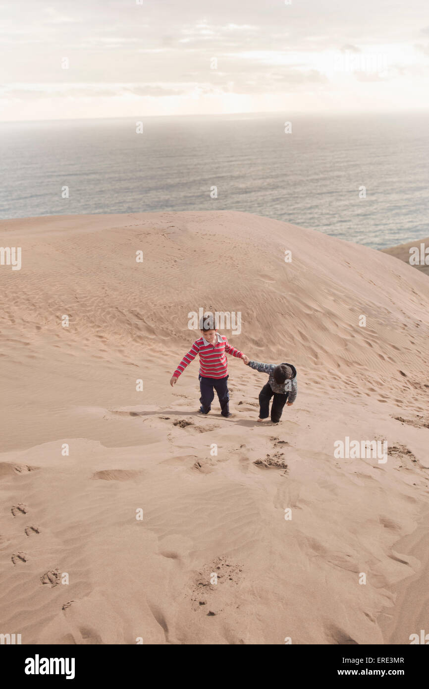 Frères hispaniques de grimper sur les dunes de sable sur la plage Banque D'Images