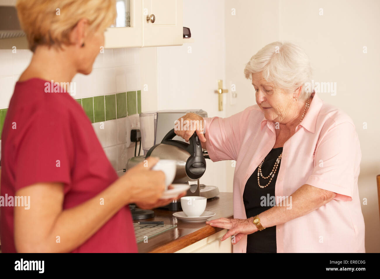 Accueil Aider à partager une tasse de thé avec Senior Woman in Kitchen Banque D'Images