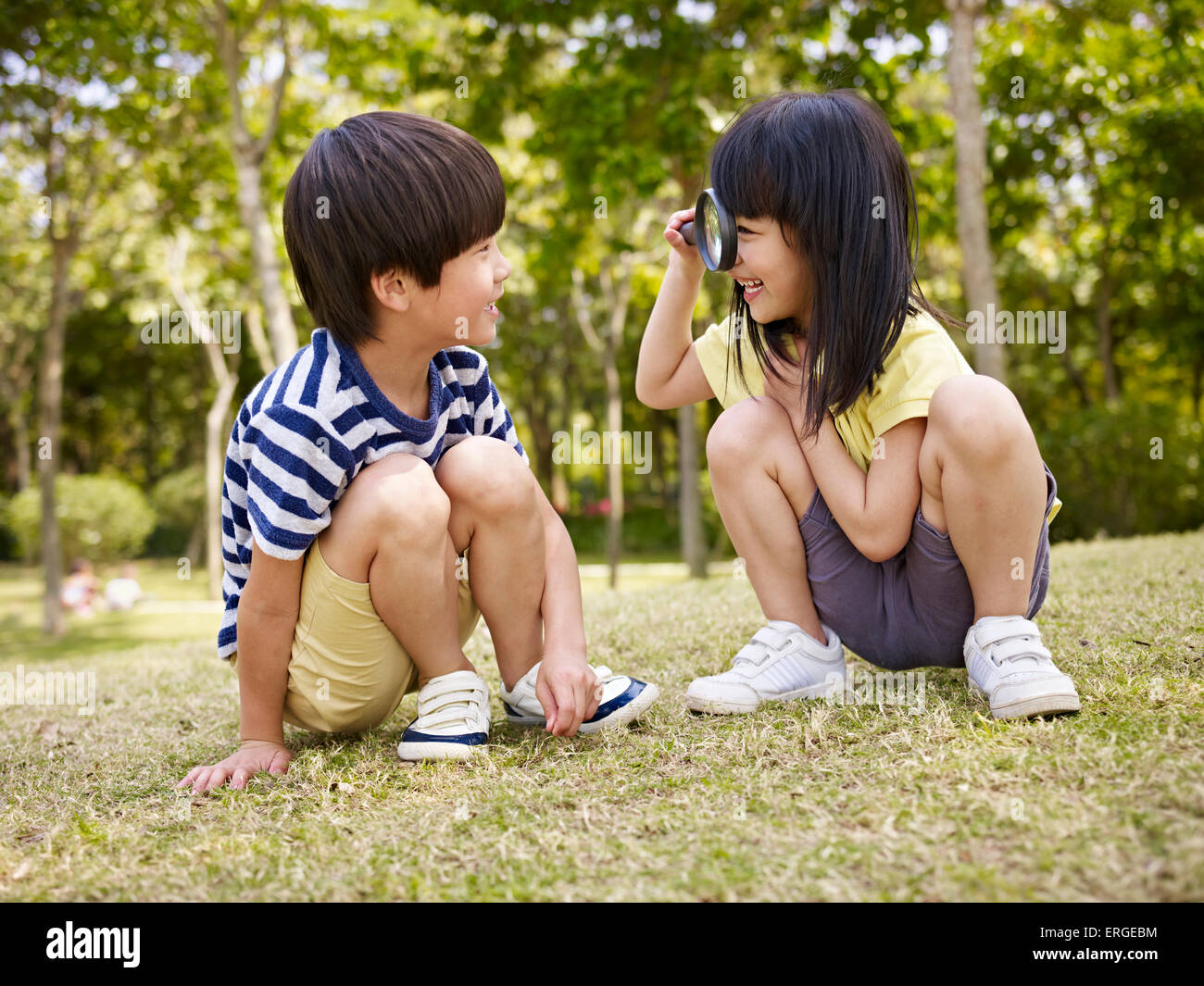 Peu à peu à la fille asiatique Asian boy à travers une loupe à l'extérieur dans un parc. Banque D'Images