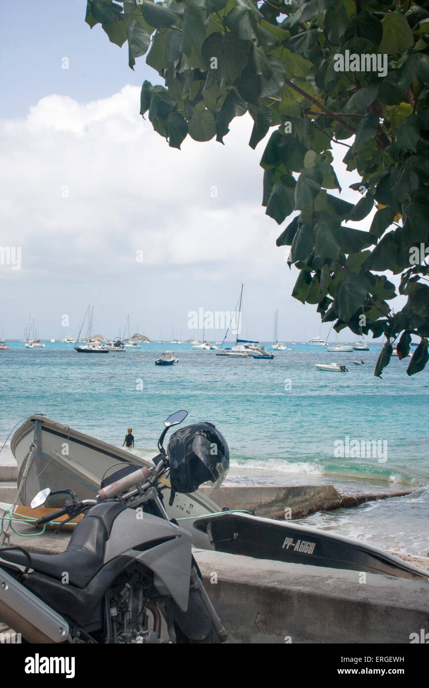 Une moto et bateaux garés à Corossol Beach à St Barth, avec la mer des Caraïbes, dans l'arrière-plan Banque D'Images