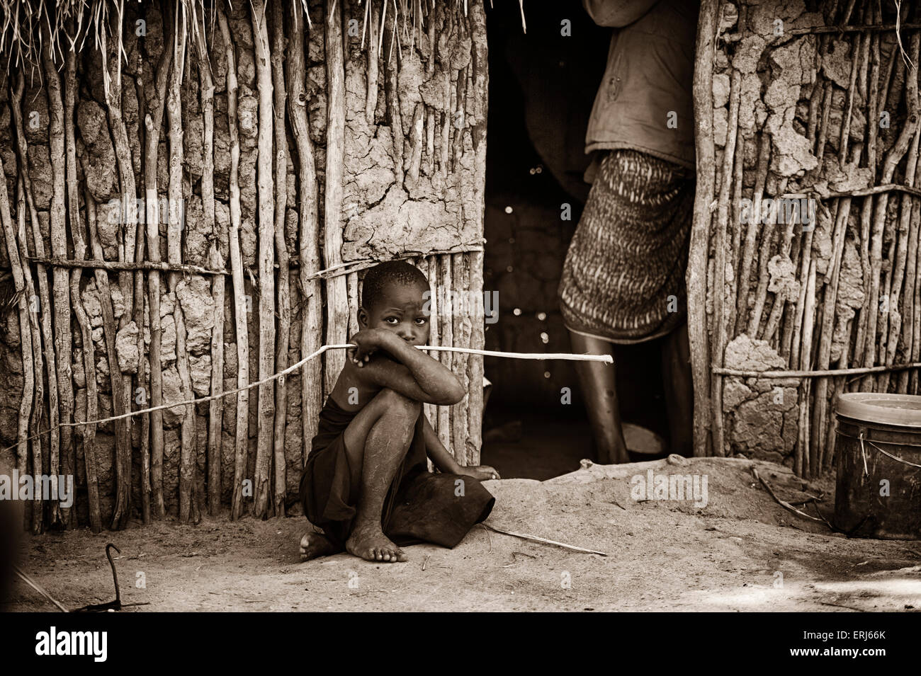 Massai garçon avec stick assis dehors, hutte de terre en Afrique Banque D'Images