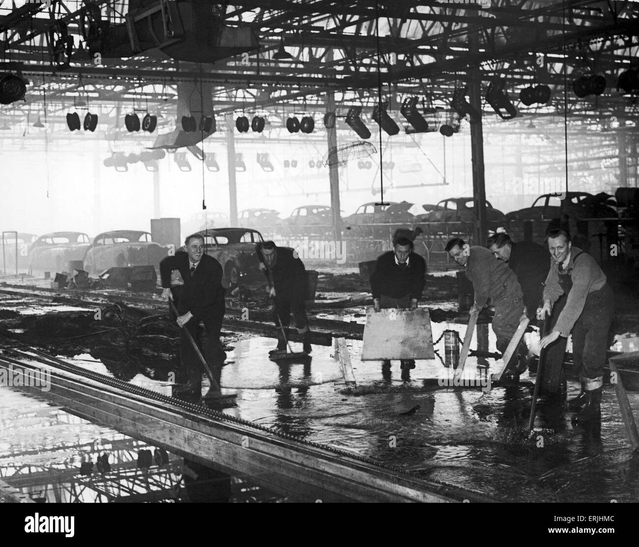 Une équipe de nettoyage va travailler balayer l'eau du bloc de l'Est de l'usine Jaguar chez Browns Lane suite à l'incendie qui détruit l'usine. 13 février 1957 Banque D'Images