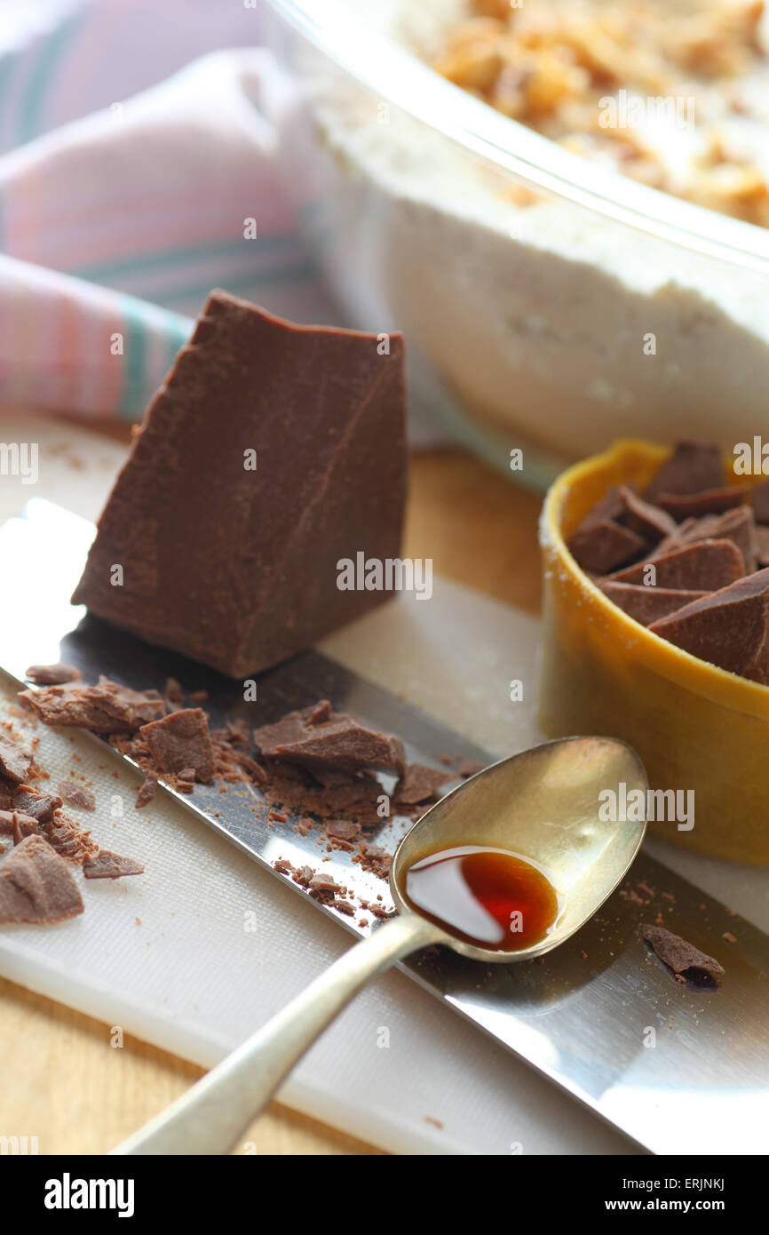 Avec des morceaux de chocolat haché sur une planche à découper avec couteau et cuillère de vanille, bol de pâte en arrière-plan Banque D'Images