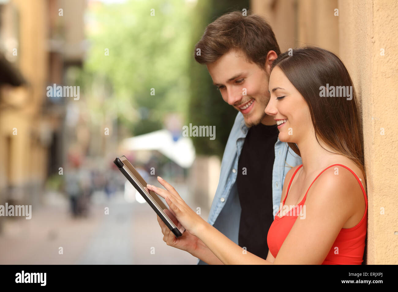 Profil d'un couple heureux parcourt une tablette dans la rue Banque D'Images