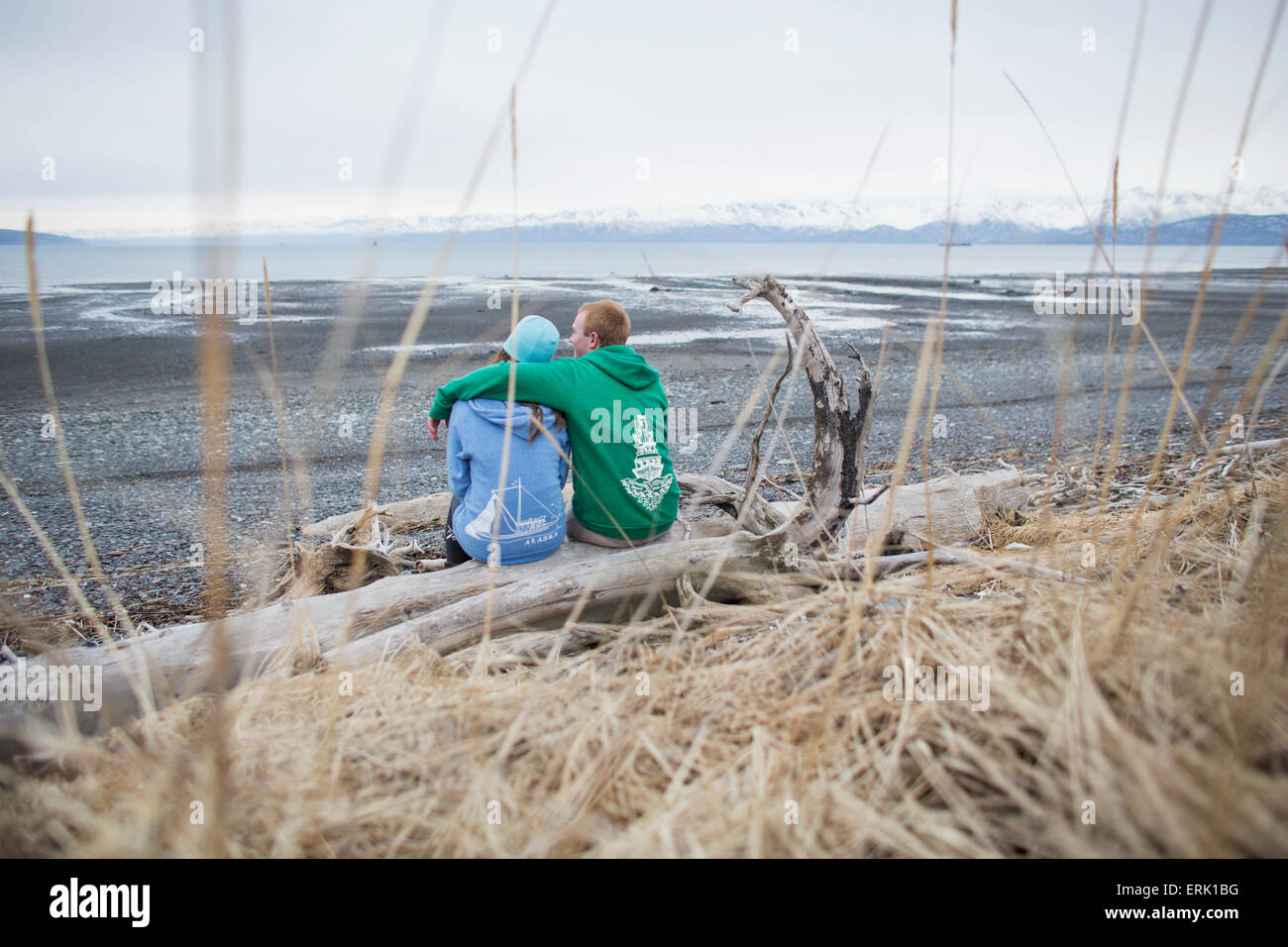 Couple assis sur du bois flotté sur la plage, Homer, Southcentral Alaska Banque D'Images