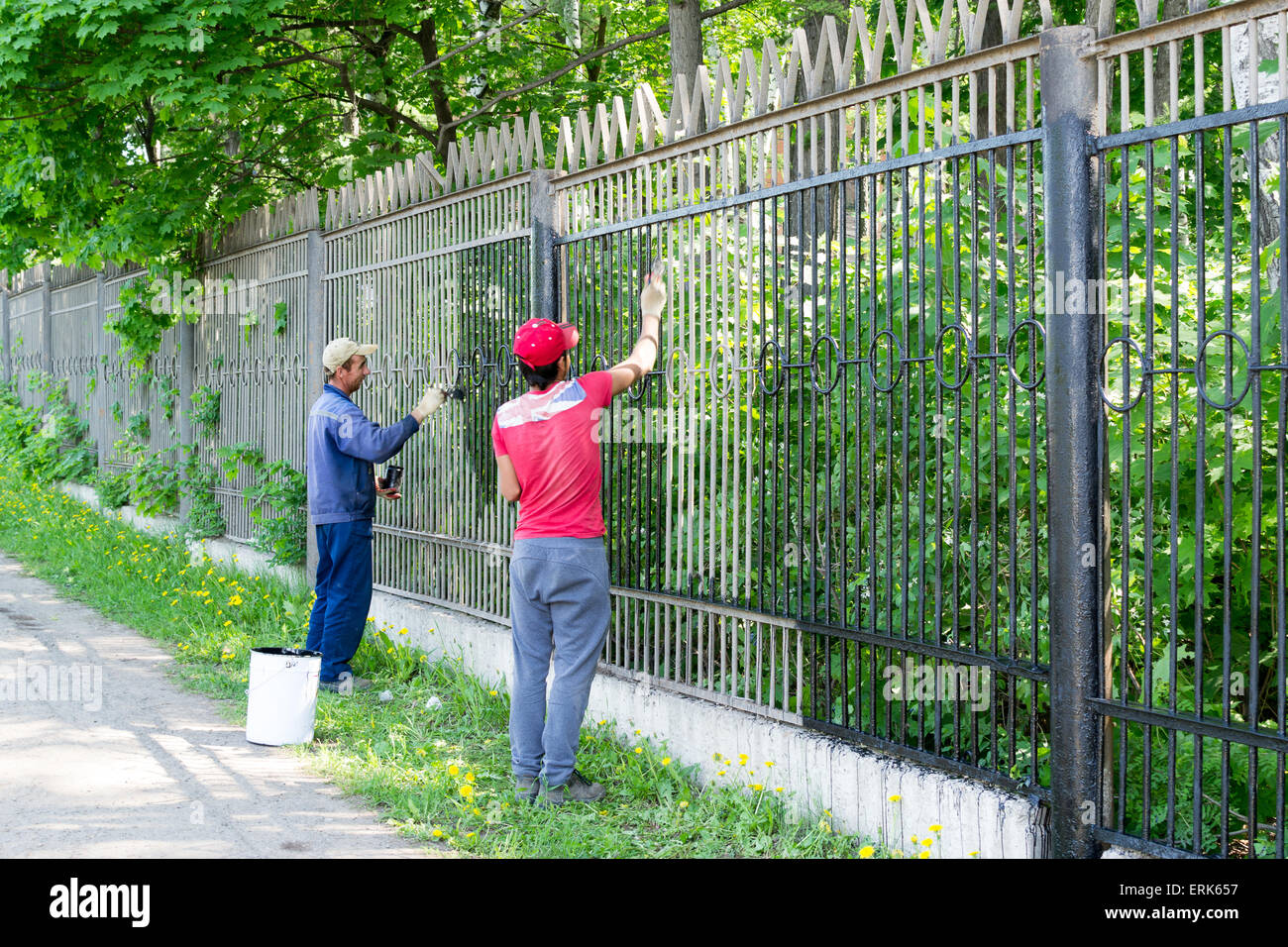 Deux travailleurs dans la ville Oufa Russie se concentrant sur la peinture d'une clôture avec la peinture dans la chaleur de l'été Banque D'Images