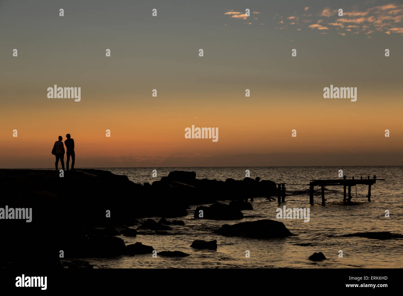 Silhouette de deux personnes debout au bord de l'eau regardant le coucher du soleil sur l'eau ; Paphos, Chypre Banque D'Images