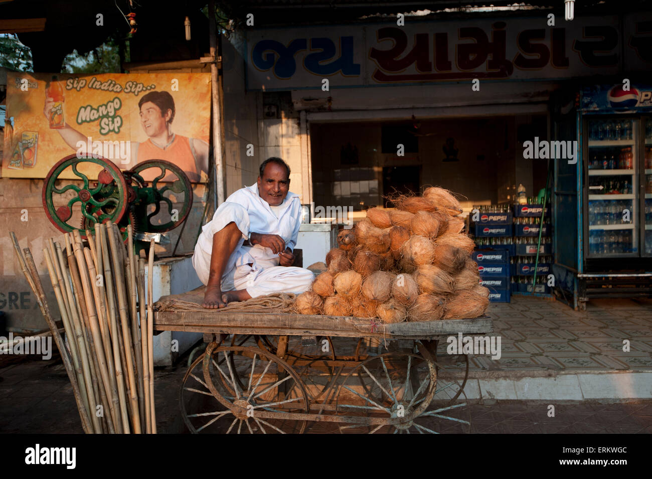Homme en blanc détendue dhoti de vendre le lait de coco et le jus de canne à sucre à partir de la simple en panier, Rajkot, Gujarat, Inde Banque D'Images