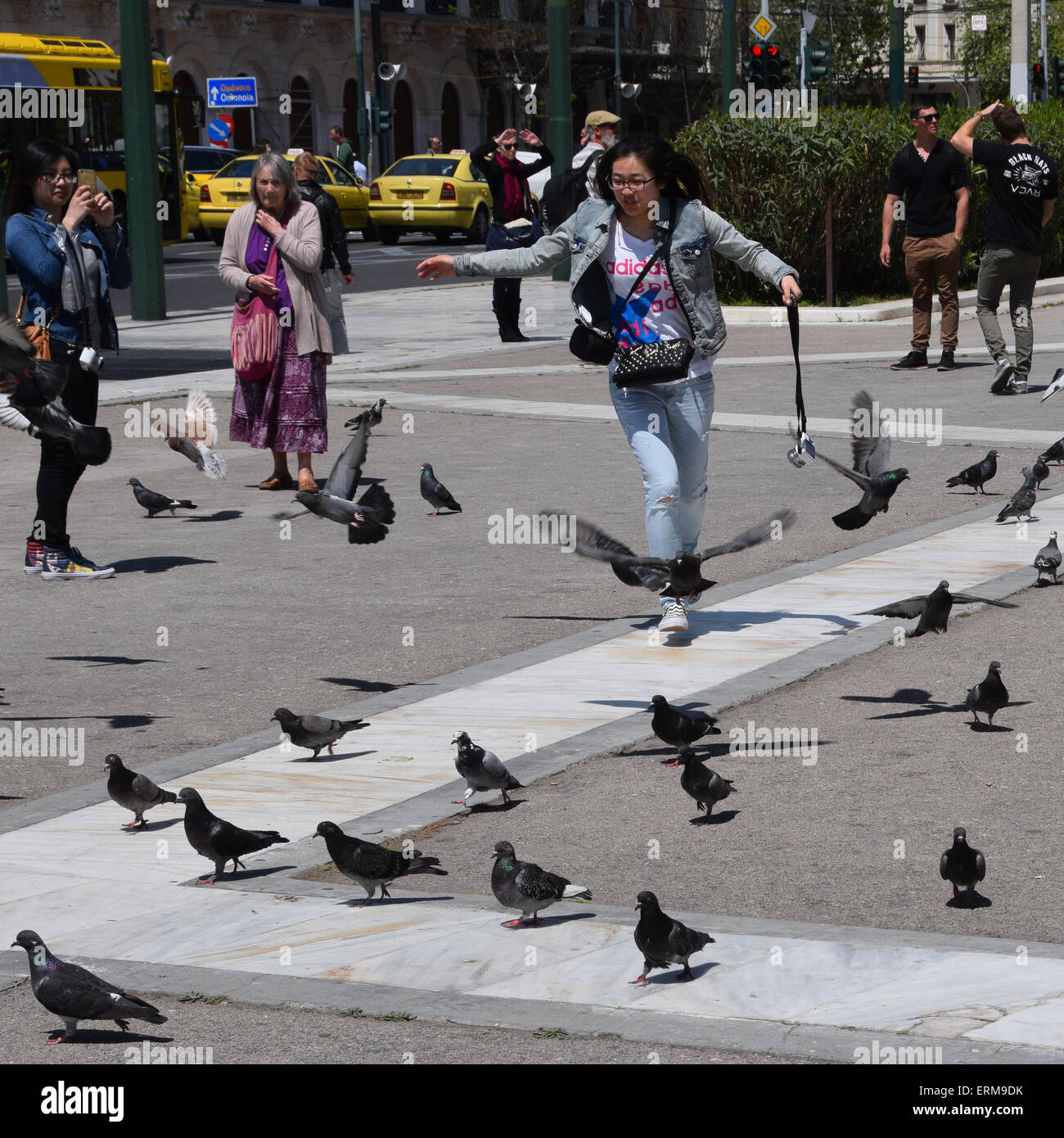 Jeune femme chassant les pigeons à la place Syntagma et les touristes profitant d'une journée de printemps ensoleillée dans le centre-ville d'Athènes, Grèce. Banque D'Images